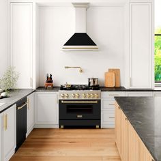 a kitchen with white cabinets, black counter tops and gold trim on the oven hood