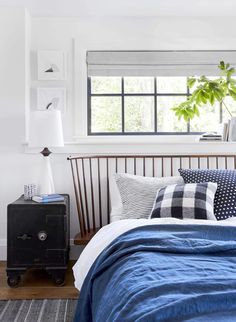 a bed with blue sheets and pillows in a bedroom next to a window that has potted plants on it