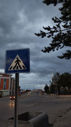 a blue and white pedestrian crossing sign sitting on the side of a road under a cloudy sky