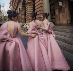 three bridesmaids in pink dresses are standing on the street and looking at each other