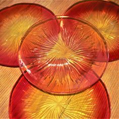 three red glass plates sitting on top of a wooden table next to an orange plate