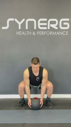 a man squats on the ground while holding a medicine ball