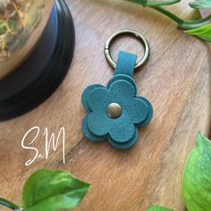 a blue leather flower keychain sitting on top of a wooden table next to a plant