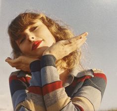 a woman holding her hand up to her face while standing in front of the sky