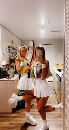 two women dressed in tennis outfits holding rackets and taking pictures with their cell phones