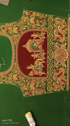 an intricately designed piece of cloth with gold and red designs on green ground next to paintbrush