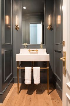 a white sink sitting under a bathroom mirror next to a wooden floor and gray walls