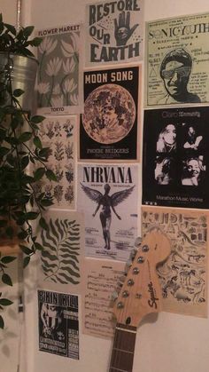 a guitar is hanging on the wall next to some posters and a potted plant