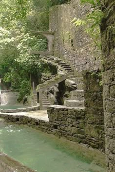 a man standing next to a river near a stone building with stairs going up it