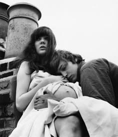 black and white photograph of two people laying next to each other on a brick wall