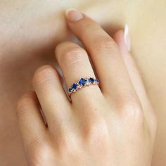 a woman's hand wearing a ring with three blue stones on the middle of it