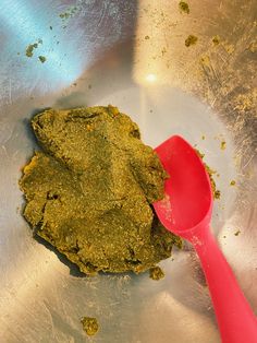 a red spatula in a metal bowl filled with green powder and other things to eat