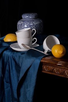 two lemons sit on a table next to cups and saucers