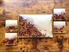 four pieces of art are displayed on a wooden table with red and white flowers in them