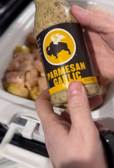 a person holding a bottle of parmesan garlic next to some food in a container