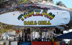 an outdoor bar and grill with tiki style umbrellas on the roof, next to palm trees