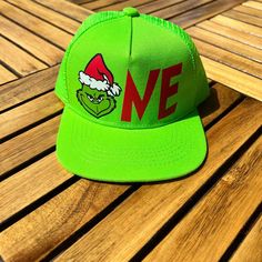 Grinch first birthday hat featuring the grinch on line green mesh snap back hat with adjustable straps. * Trendy Mesh Snap Back Hats * Features a Firm Rectangular Brim * 100% Polyester * 48 cm Circumference * Snap Back Closure Green Fitted Hat With Flat Bill, He’s A Mean One First Birthday Grinch, Green Snapback Hat With Letter Print, Green Fitted Hat With Embroidered Logo, Christmas 1st Birthday, Green Hats With Embroidered Logo, One Size, Snap Back Hats, First Birthday Hat, Snap Back Hat