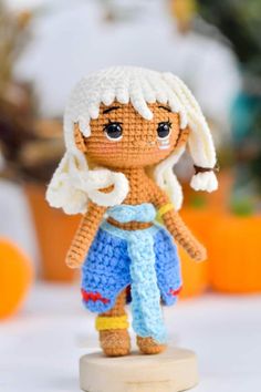 a small crocheted doll is standing on a wooden stand with pumpkins in the background