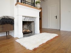 a living room with a fire place and white rugs on the wooden flooring