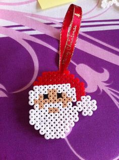 a cross stitch christmas ornament hanging from a red ribbon on a purple background