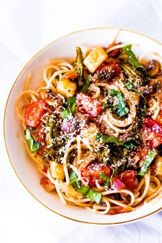 a bowl filled with pasta and vegetables on top of a white table cloth next to a fork