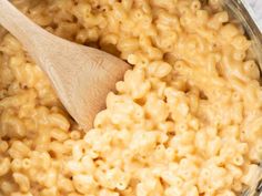 macaroni and cheese is being stirred with a wooden spoon in a glass bowl