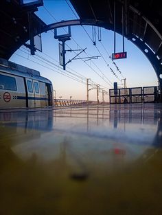 an empty train station with two trains on the tracks and one in the distance, at sunset