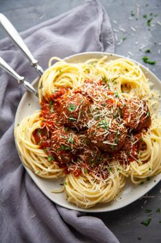 a plate of spaghetti with meatballs and parmesan cheese on top, next to a fork