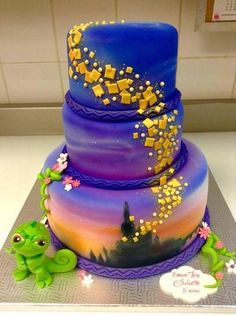 a three tiered cake decorated with purple and yellow icing, topped with a frog figurine