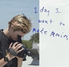 a man holding a camera next to a white board with writing on it that says, 1 day i want to make movies