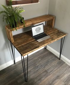 a laptop computer sitting on top of a wooden desk next to a potted plant