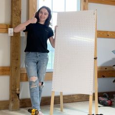 a woman standing in front of a white board with holes on it and giving the thumbs up