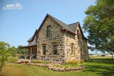 an old stone house sits in the middle of a grassy area with trees and flowers