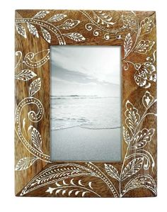 an ornate wooden frame with white flowers and leaves on the edge, in front of a beach