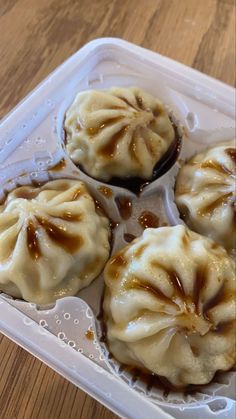 four chinese dumplings in a plastic container on a wooden table, with sauce drizzled over them