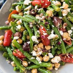 a white plate topped with green beans, tomatoes and feta cheese on top of it