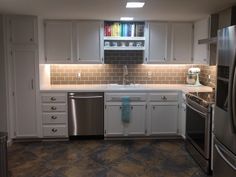 a kitchen with white cabinets and stainless steel appliances in the center, along with tile flooring