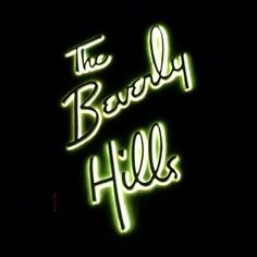 the beverly hills sign lit up at night with neon lights on it's side