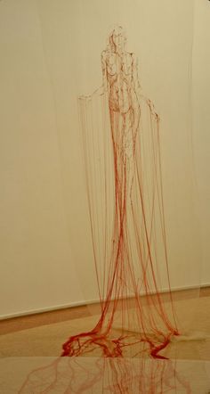 a red sculpture sitting on top of a floor next to a white wall