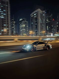 a car driving down the road in front of tall buildings at night with lights on