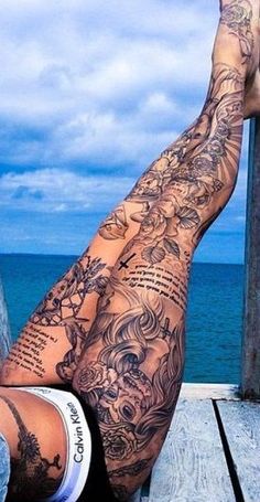 a man laying on top of a wooden dock next to the ocean with tattoos on his legs