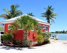 a small red house sitting on top of a beach next to palm trees and water