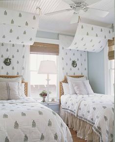 two beds in a bedroom with white and blue wallpaper, one has a fan on the ceiling