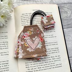 an open book with some flowers on it next to a pair of hair clips and a flower bouquet