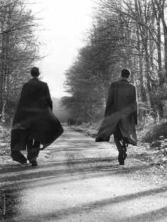 two people walking down a dirt road in the woods