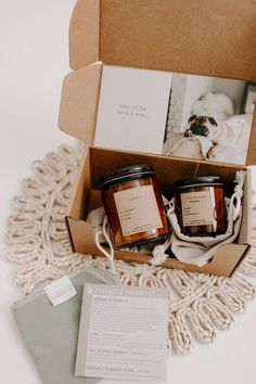 two jars of candles in a box on a white table cloth next to an envelope