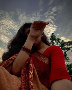 a woman wearing a red and gold sari holding her hand up to her face