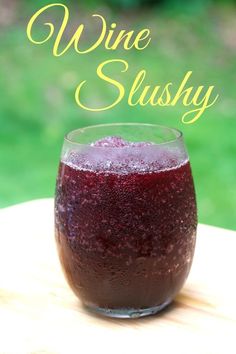 a glass filled with red liquid sitting on top of a wooden table next to green grass