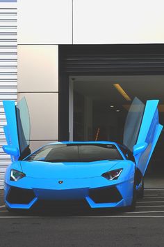 a blue sports car parked in front of a garage with its doors open and it's door opened