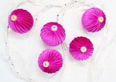 four pink paper flowers sitting on top of a clear plate with string lights around them